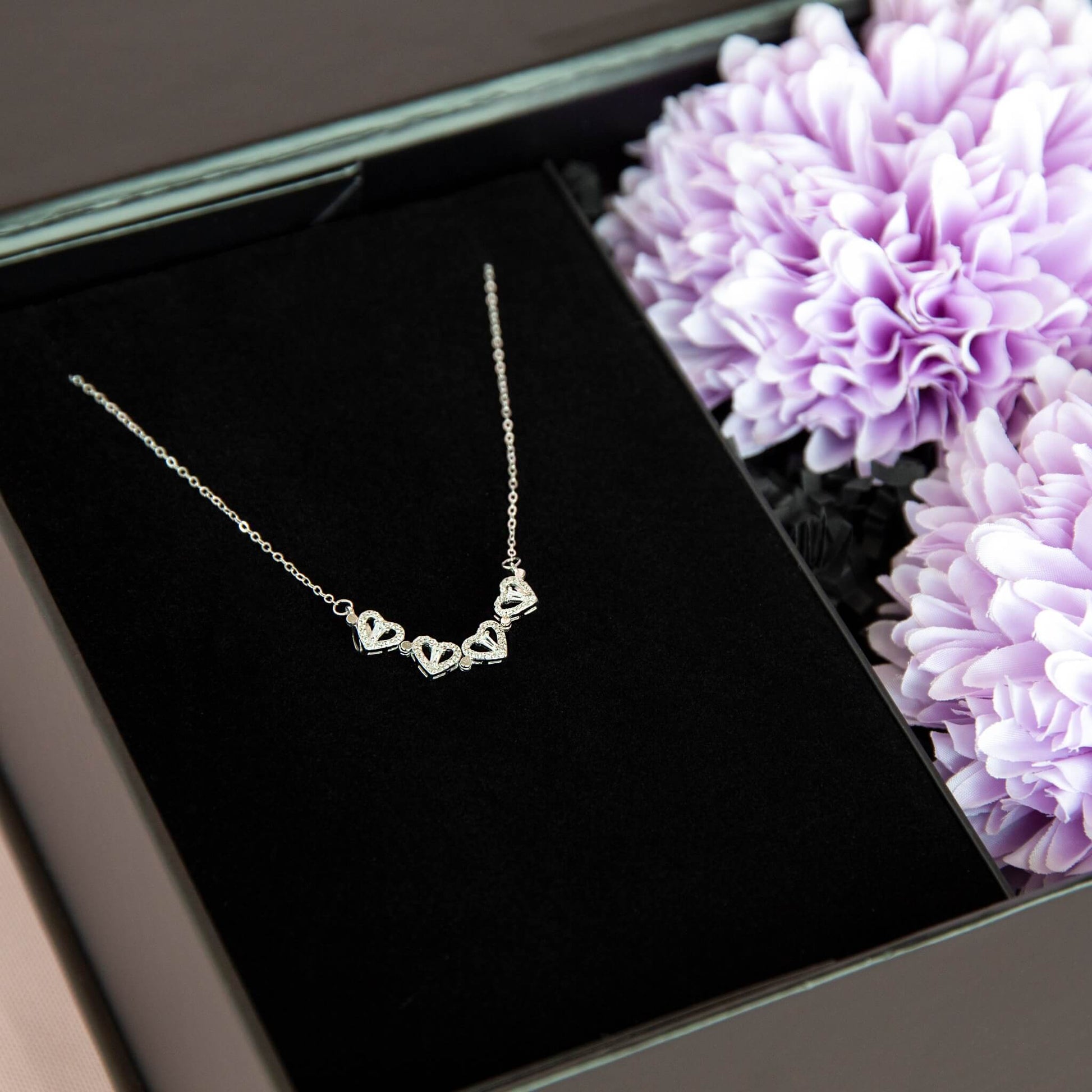 Detlajbilde av hjertesmykke i sterling silver og zirkonia stener. Fint plassert i en gaveeske fra Boxit med lilla blomster.