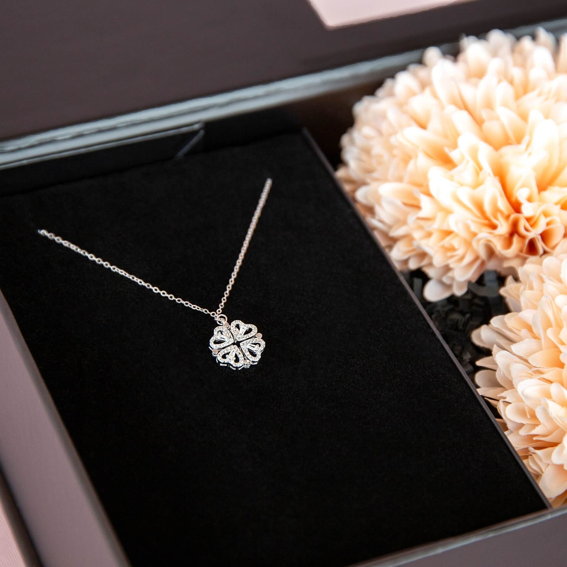 Detlajbilde av et sammenslått hjertesmykke i sterling sølv. Fint pakket i en sort gaveeske fra Boxit med ferksenfarget blomster.