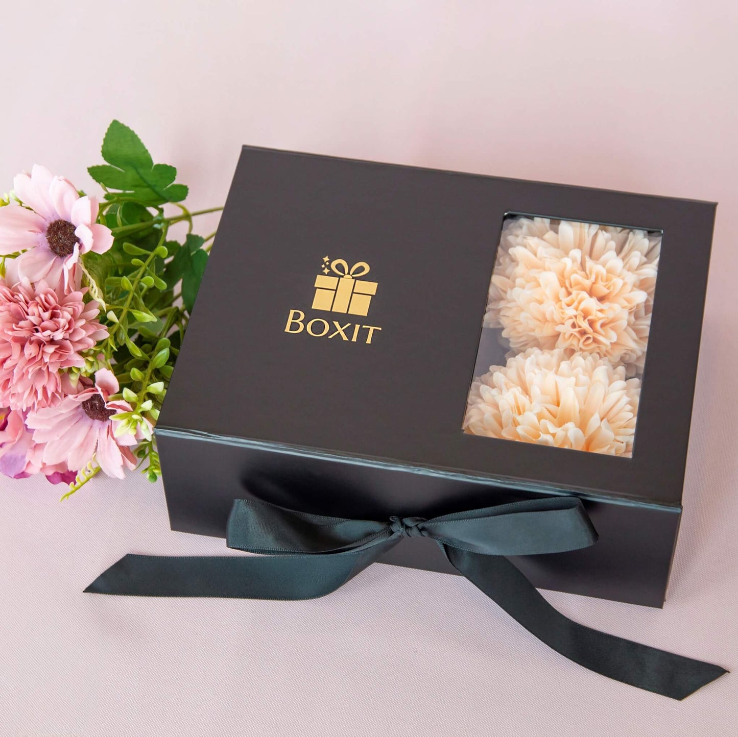 Lukket sort gaveeske fra Boxit med gulllogo og fersken fargede blomster. Gave klar til å gis til henne.