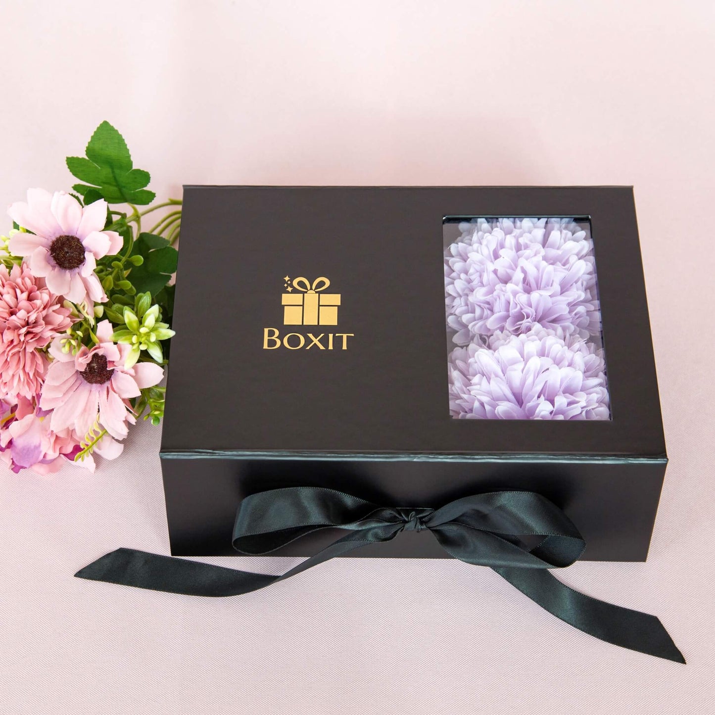 Lukket sort gaveeske fra Boxit med gulllogo og lilla blomster. Gave klar til å gis til henne.