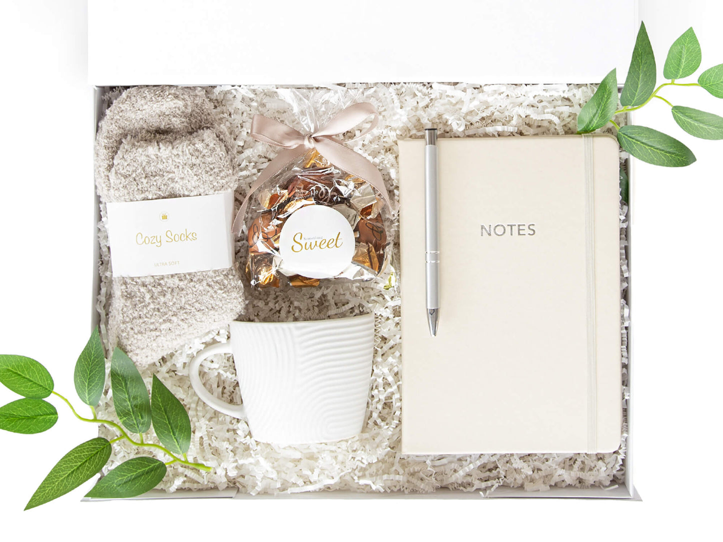 Beige notatbok, myke sokker, deilig sjokolade og en hvit kopp. Pakket i en hvit gaveeske klar til å gis bort i gave.