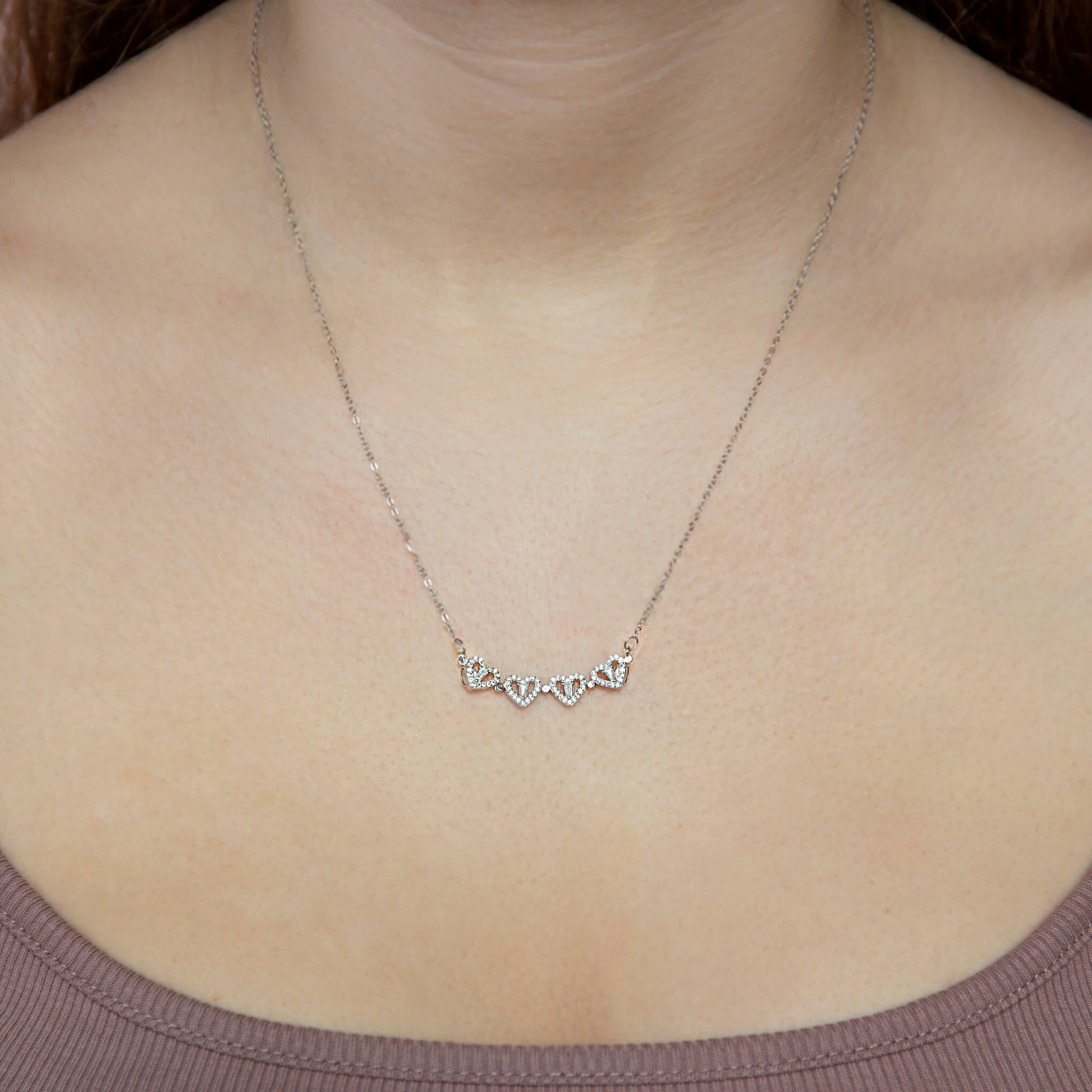 Smykke med 4 hjerter på rad i sterling sølv med zirkonia stener rundt halsen på kvinne. Elegant gave til henne