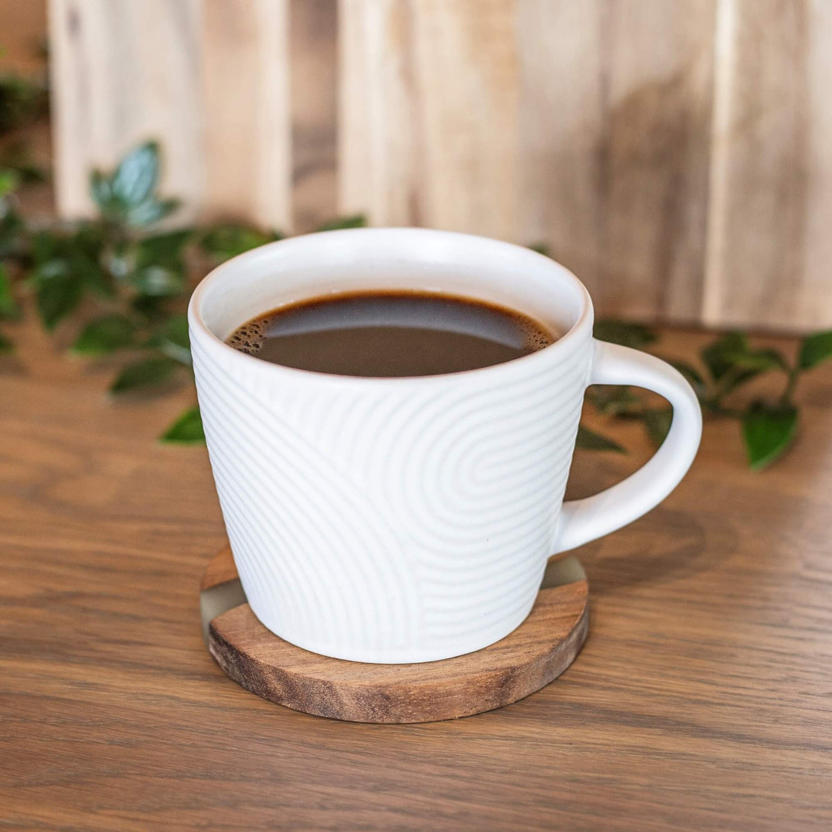 Hvit kaffekopp med strukturert mønster på rund bordbrikke i akasietre