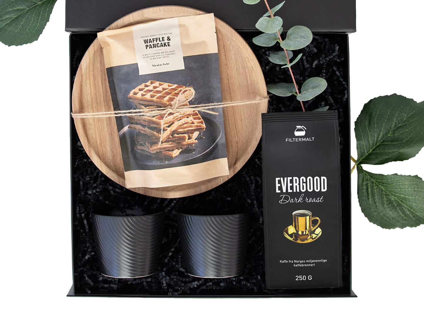 Svart gaveeske med kaffe, kopper, serveringsfat og vaffelmix.