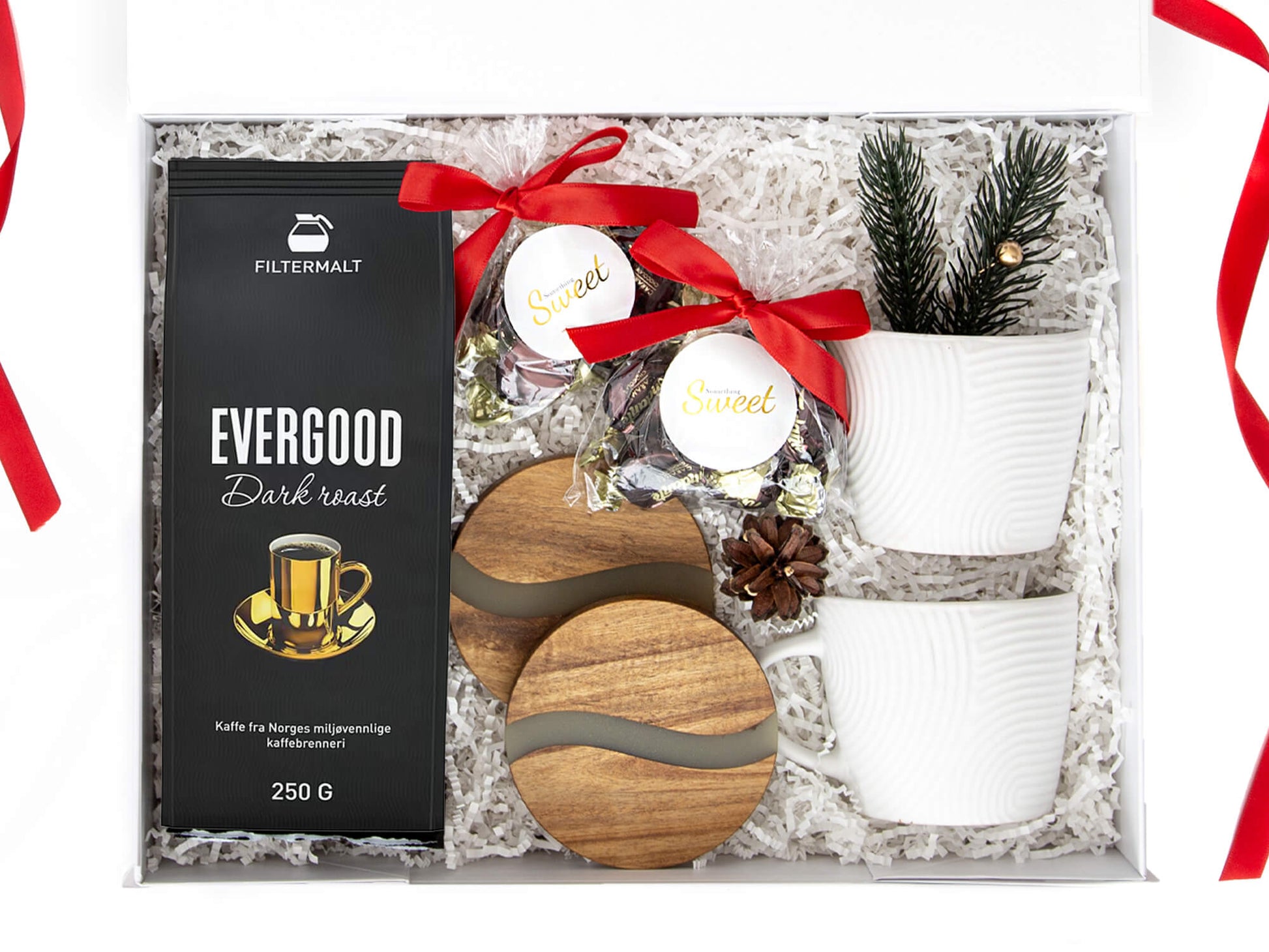 Julegave med kaffe, sjokolade, bordbrikker og hvite kopper i en hvit gaveeske.