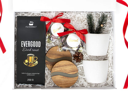 Julegave med kaffe, sjokolade, bordbrikker og hvite kopper i en hvit gaveeske.