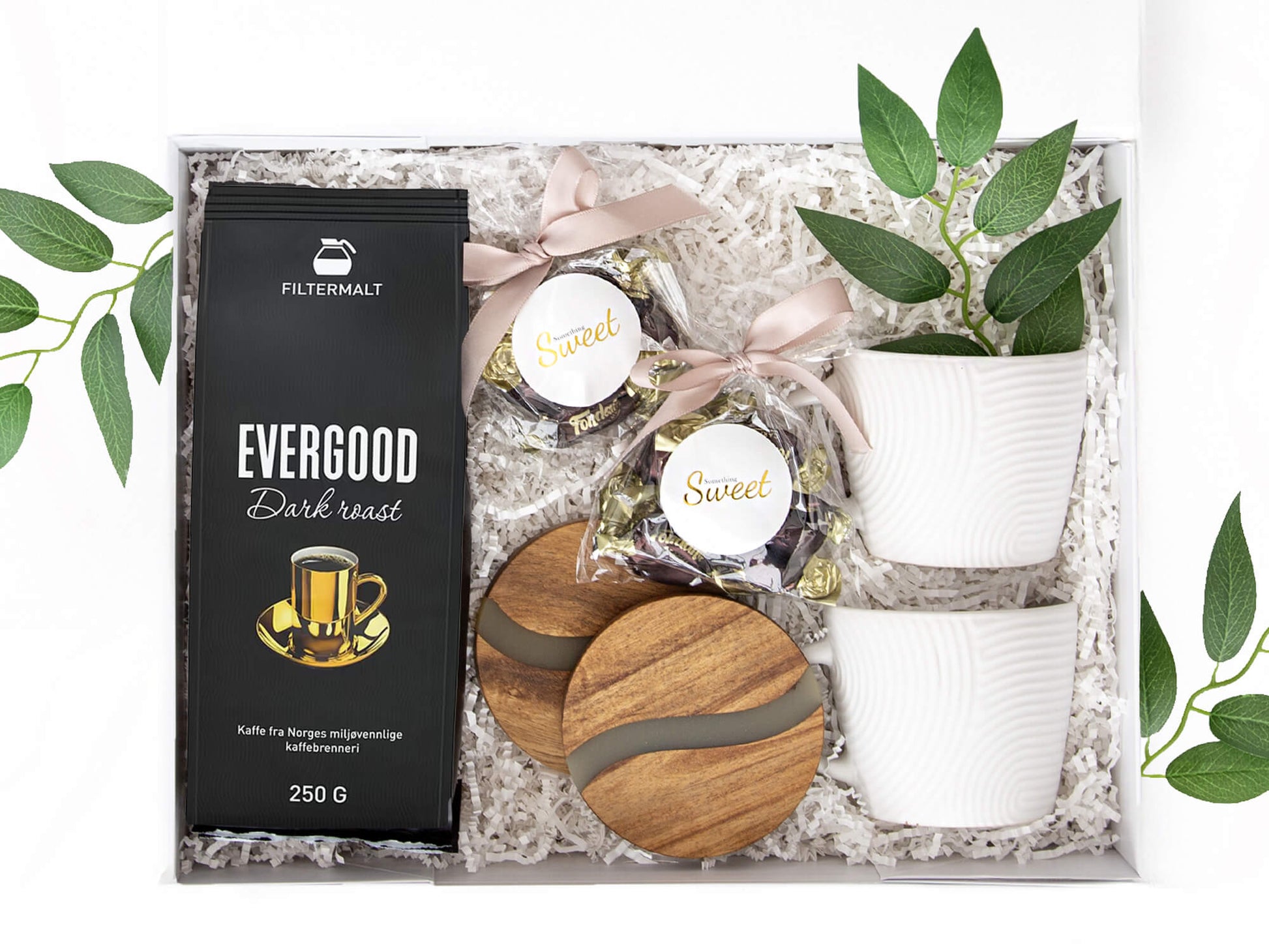 Gave med kaffe, sjokolade, bordbrikker og hvite kopper i en hvit gaveeske.