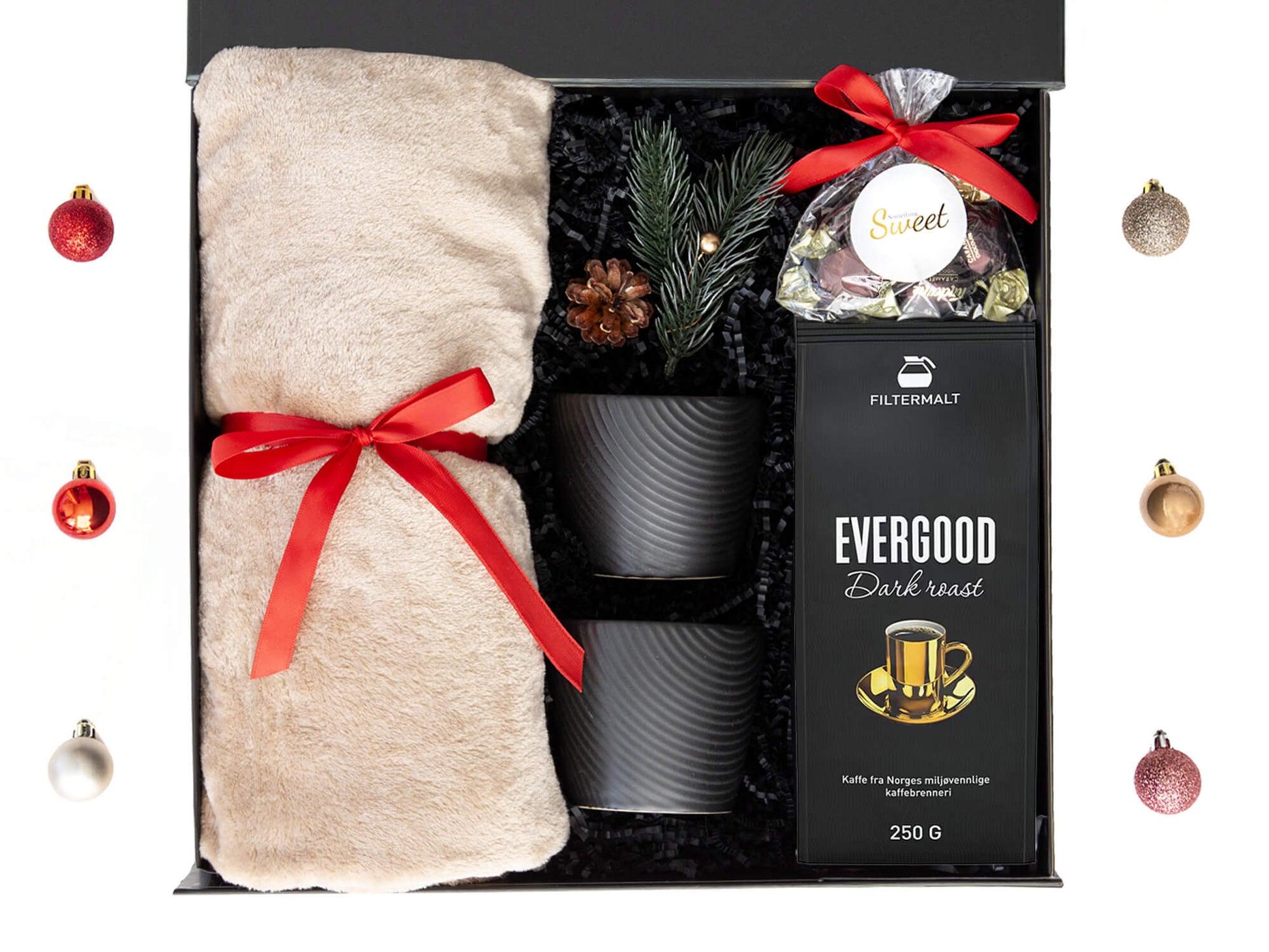 Svart gaveeske med kaffe, kopper, mykt pledd og sjokolader. Dekorert med juledekor.