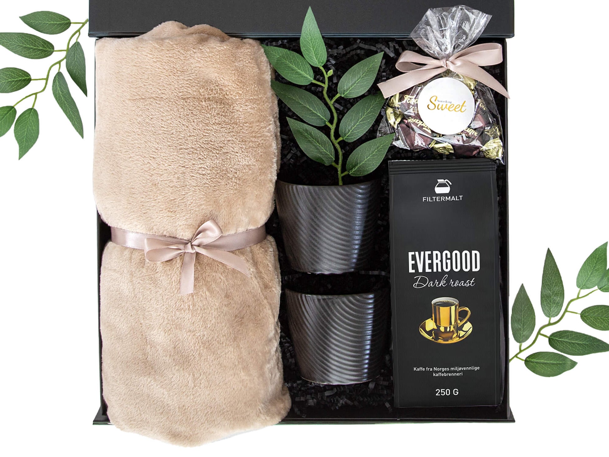 Svart gaveeske med kaffe, kopper, mykt pledd og sjokolader.