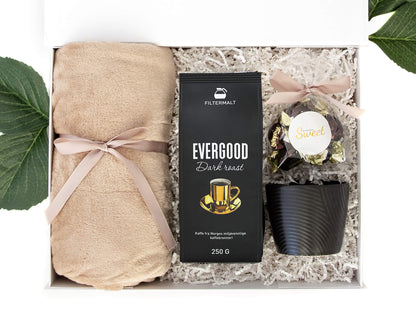 Supermykt pledd, utsøkt kaffe, fondant sjokolade og svart kopp. Alt pakket i en hvit gaveeske.
