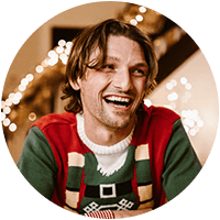 Ung mann i julegenser som smiler foran juledekorasjon.