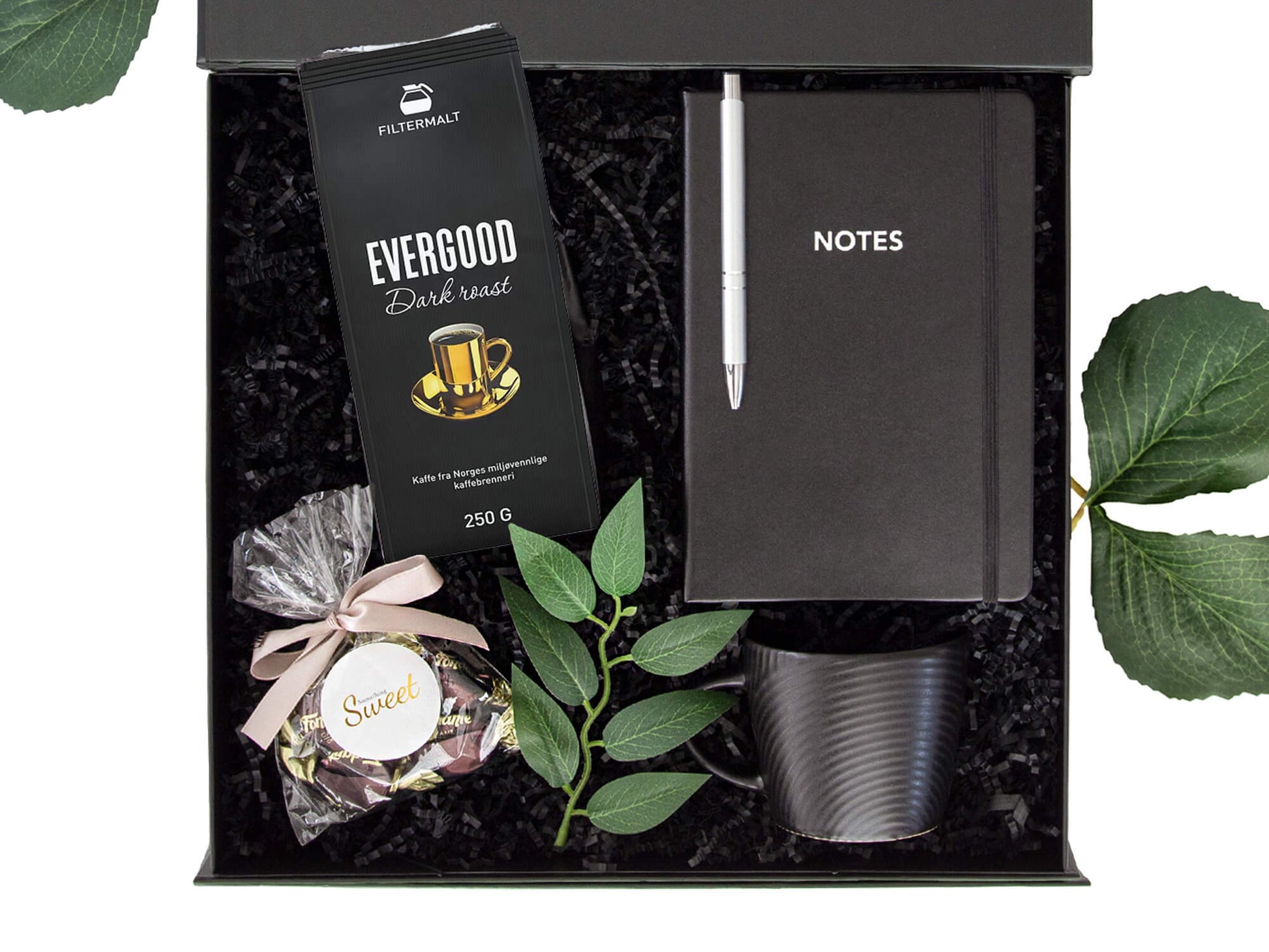 Svart gaveeske med kaffe, kopp, notatbok og sjokolader.