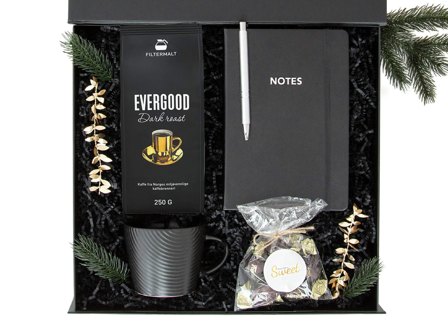 Svart gaveeske med kaffe, kopp, notatbok og sjokolader. Dekorert med juledekor