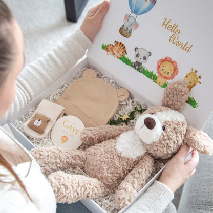 En gaveeske med kosebamse, babylue og babysokker som blir åpnet.