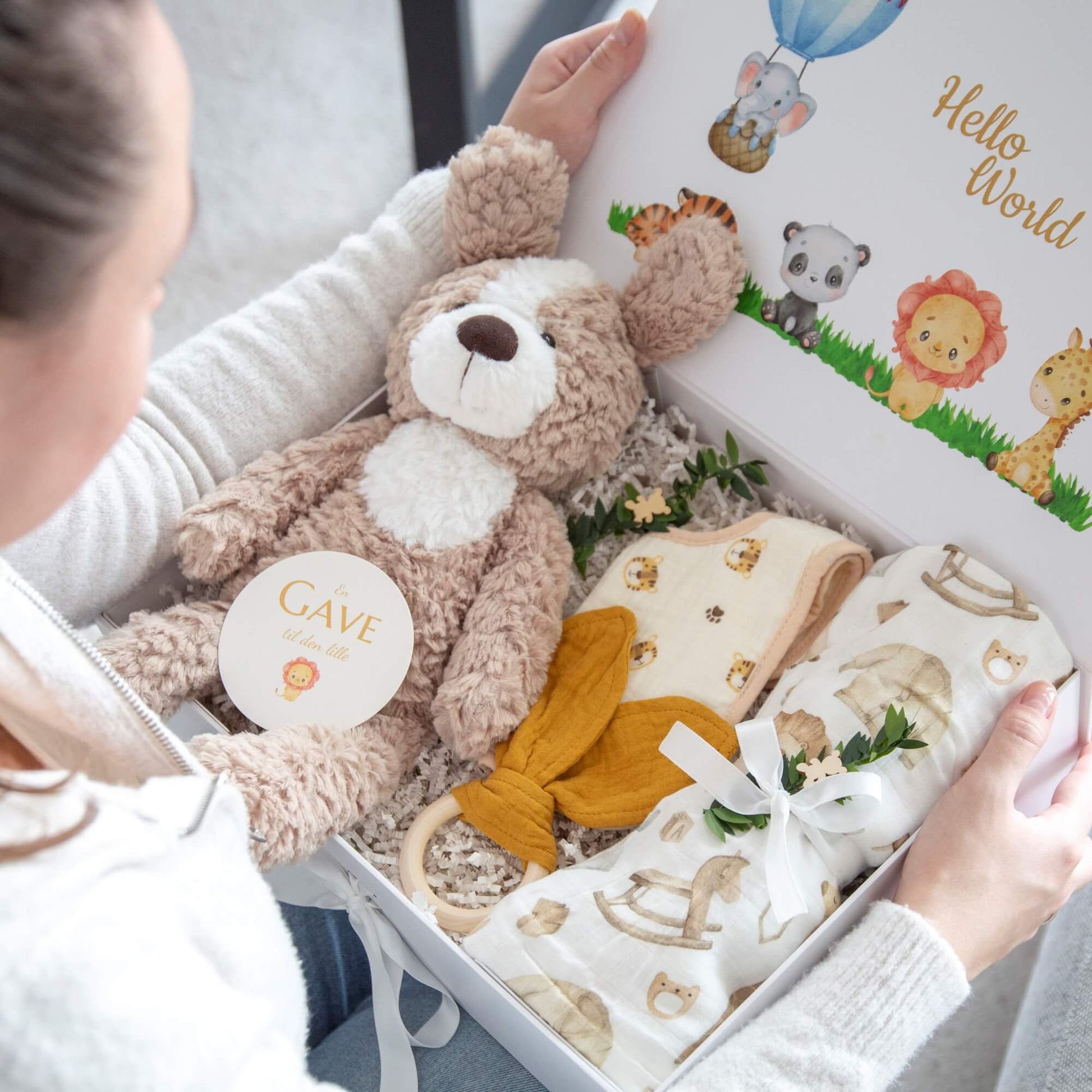 En babygave blir åpnet som inneholder kosebamse, babypledd, smekke og babyrangle.