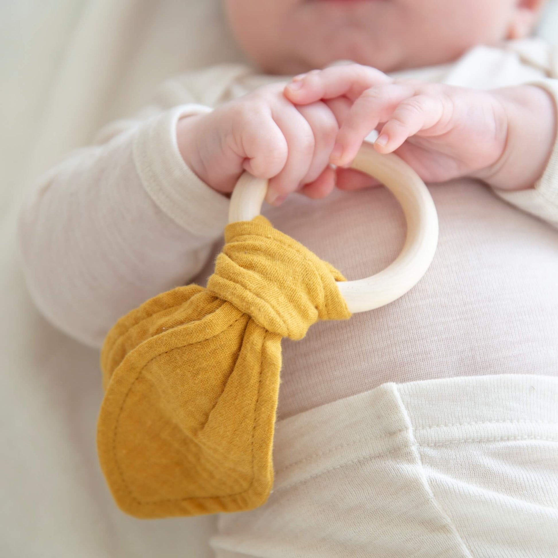 Baby som leker med en rangle med trehåndtak og bomull detaljer.
