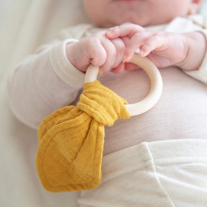 Baby som leker med en rangle med trehåndtak og bomull detaljer.