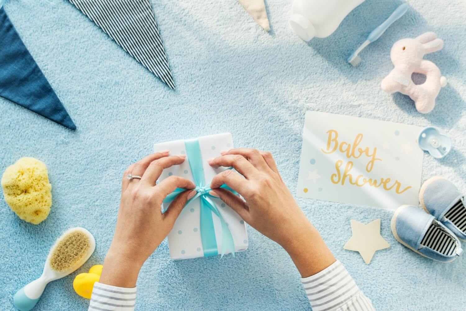 Babyshower gaveinnpakking med blått bånd, gaveeske, babysko, leker og dekorasjoner.