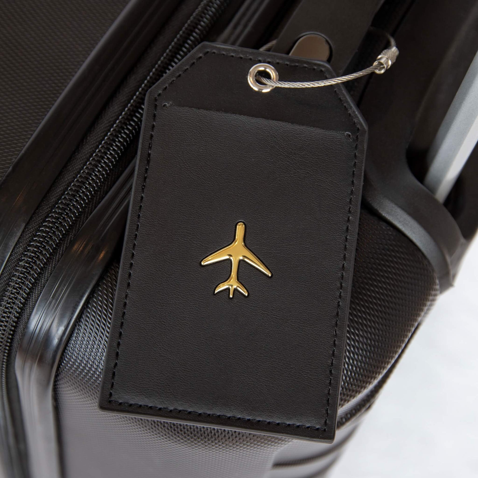 Bagasjelapp i sort lær med et gull fly på. Et produkt i reisegaveesken til henne.