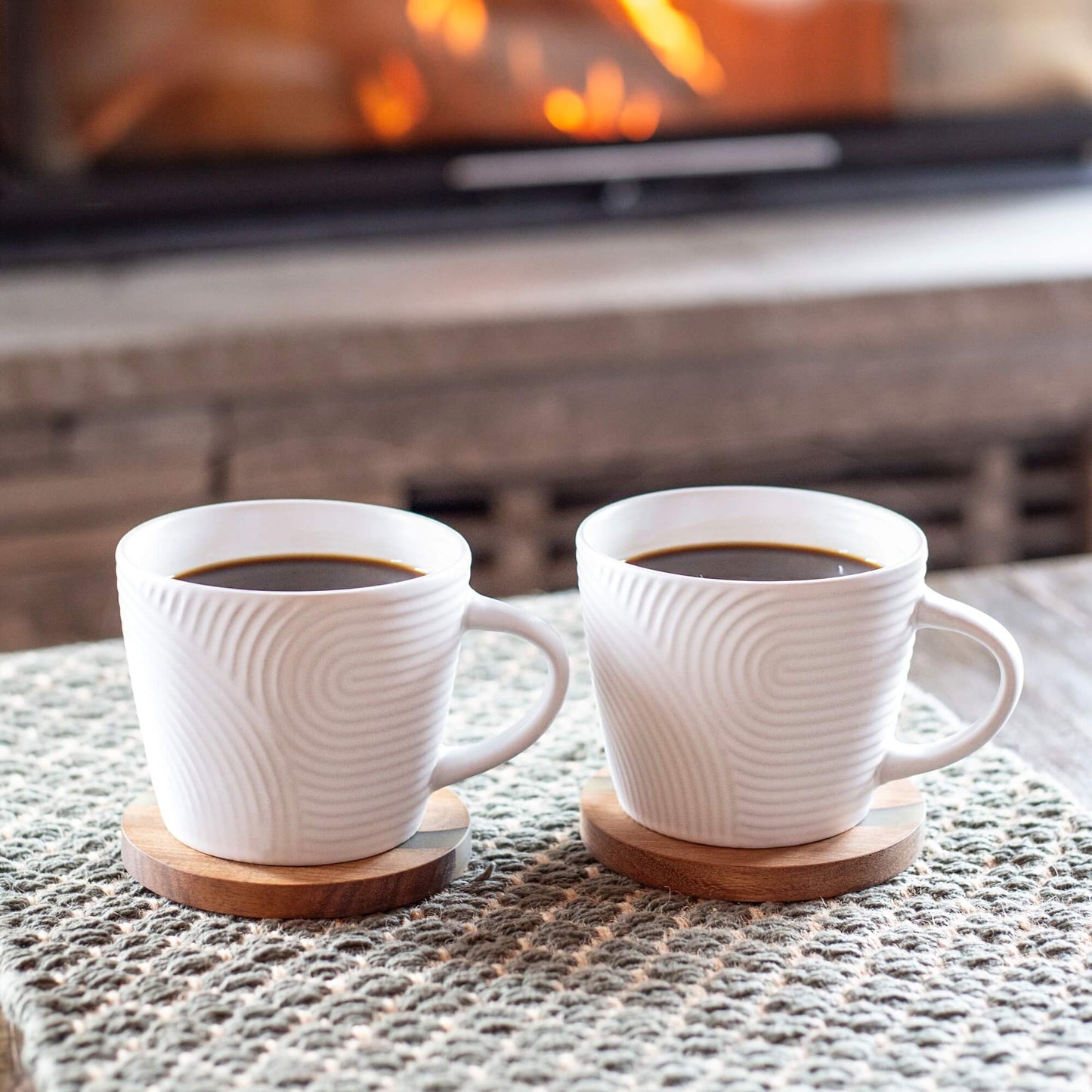 To hvite kaffekopper med strukturert mønster på bordbrikker i tre