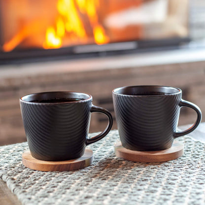 To sorte kaffekopper med strukturert mønster foran en peis