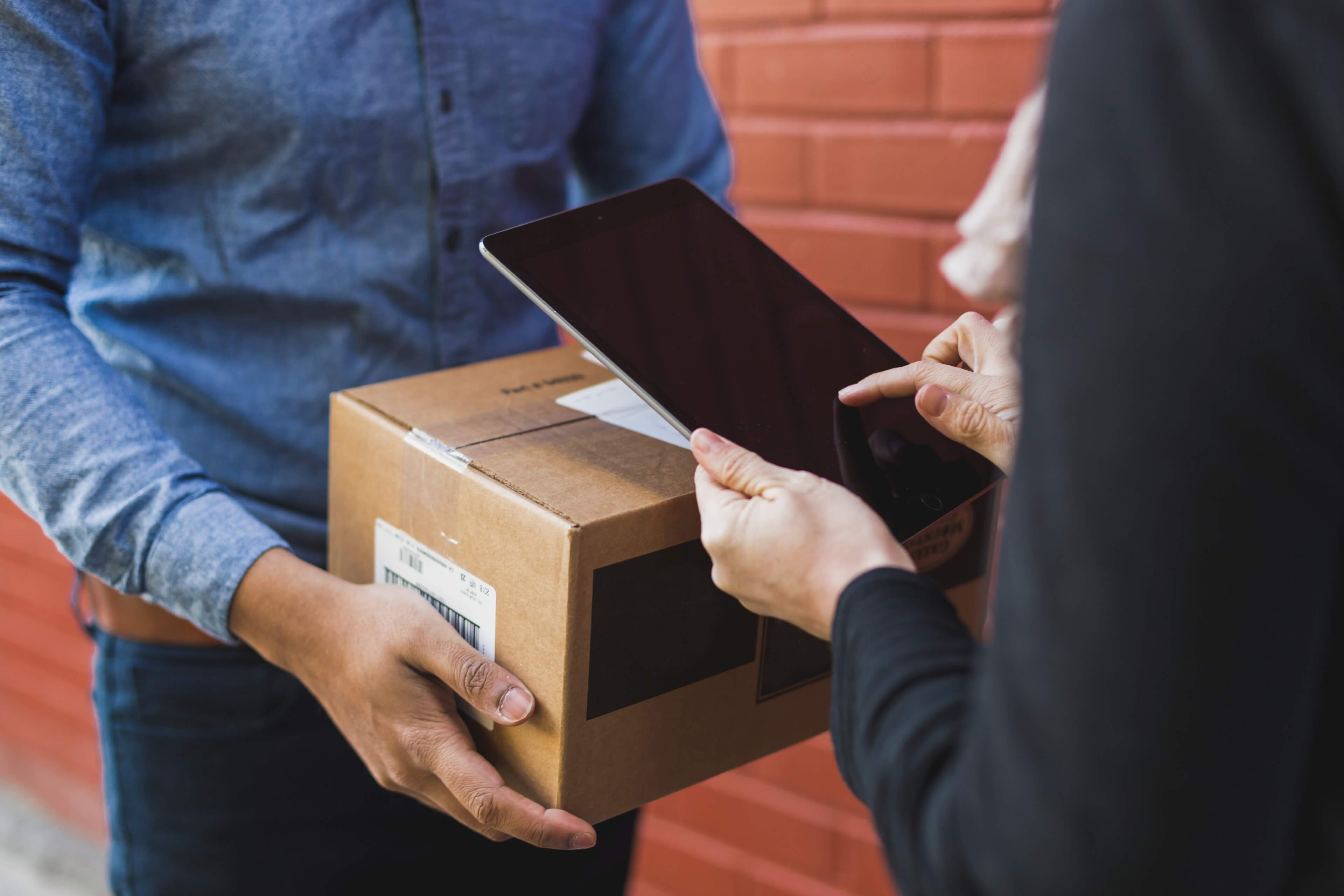 Levering av pakke der mottaker signerer på nettbrett ved utlevering, illustrerer frakt og leveringstid