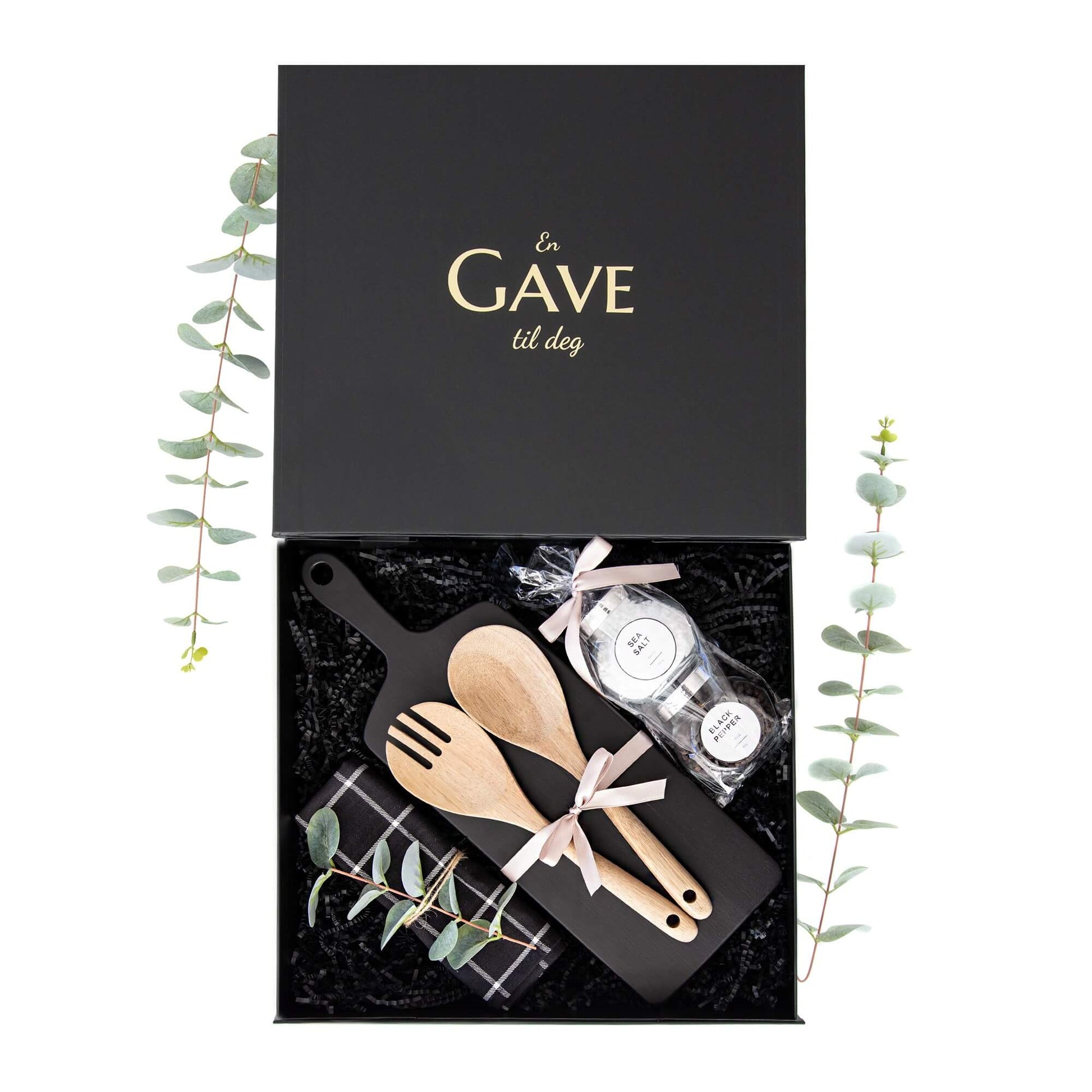 Sort åpen gaveeske med serveringsbrett, krydder og flere kjøkken artikler.