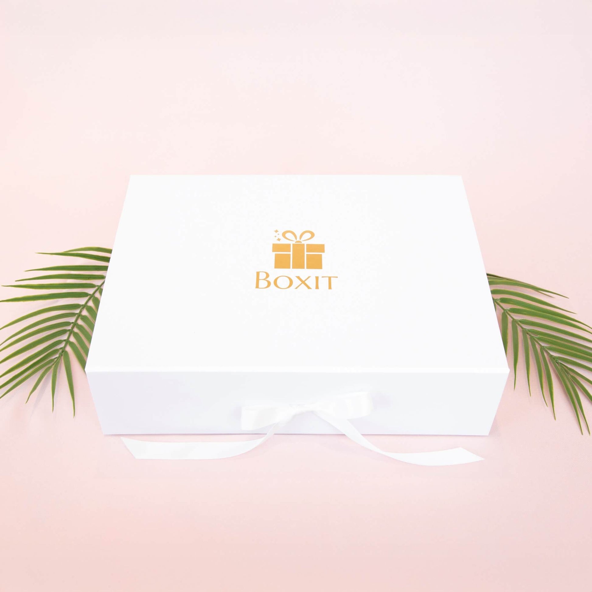 Lukket hvit gaveeske med gullfarget Boxit-logo og hvit silkebånd – elegant gaveinnpakning til dame.