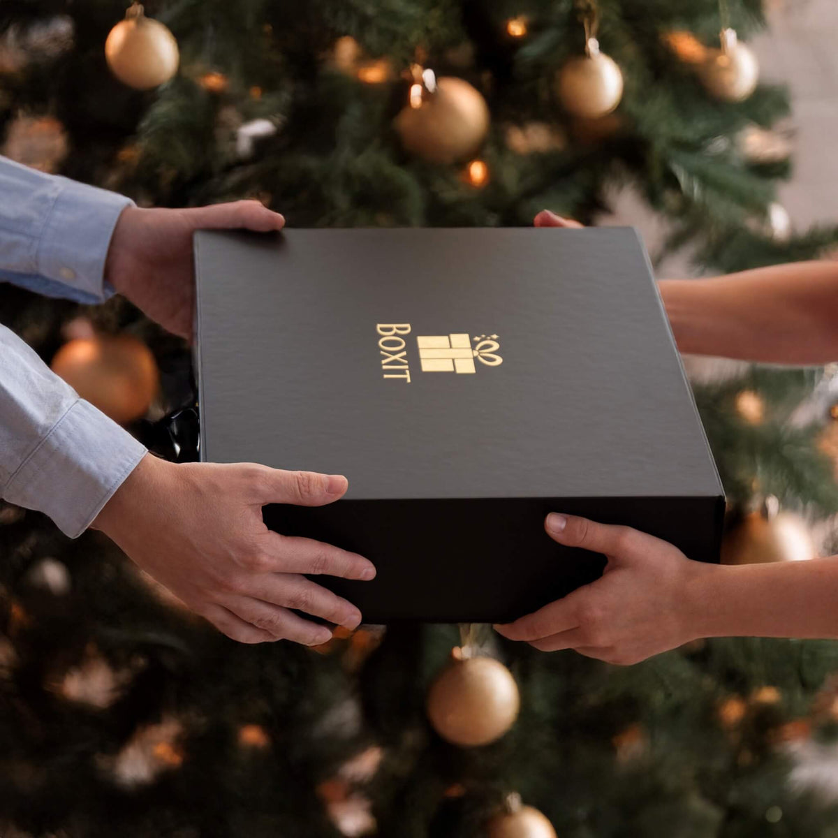 Utveksling av julegaver ved juletreet. Eksklusiv svart gaveeske fra Boxit.