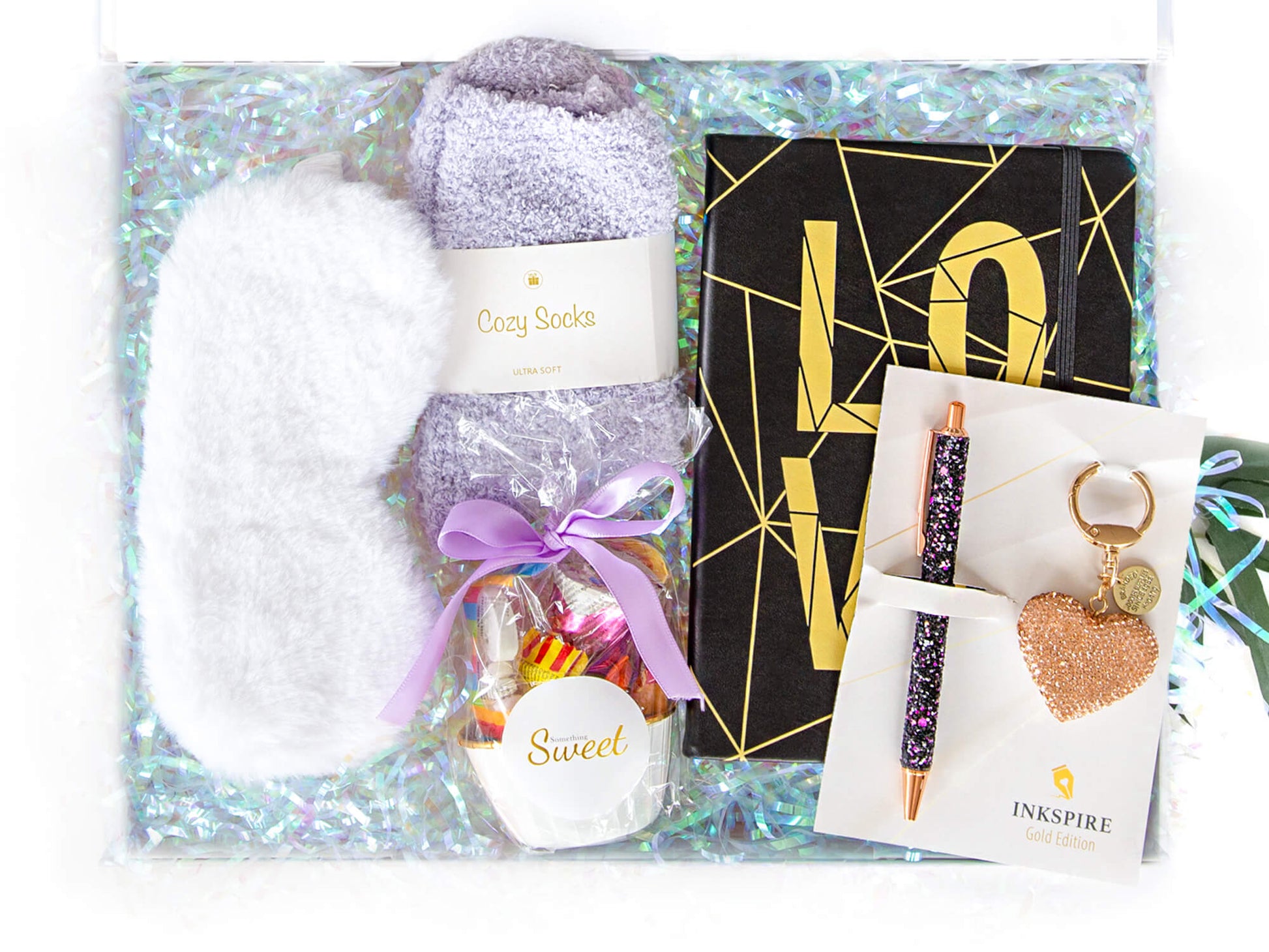 Gaveeske med notatbok, fluffy sokker og sovemaske, sjokolader og glitter penn og nøkkelring.