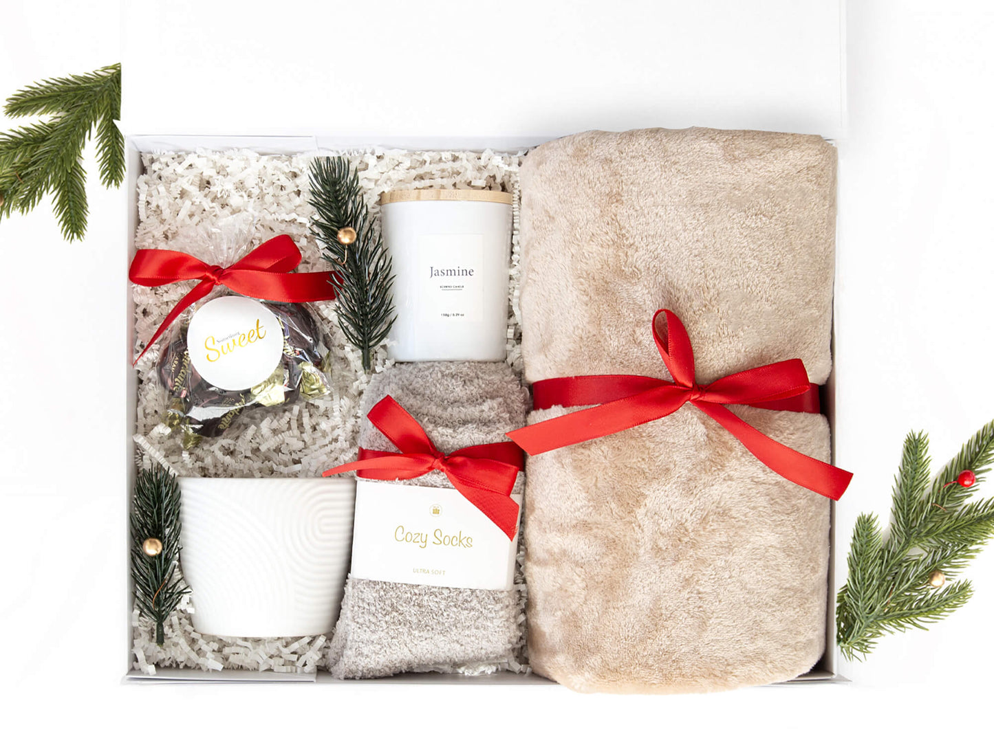 Hvit gaveeske med mykt pledd, sokker, duftlys, kopp og utsøkte sjokolader. Dekorert med juledekor