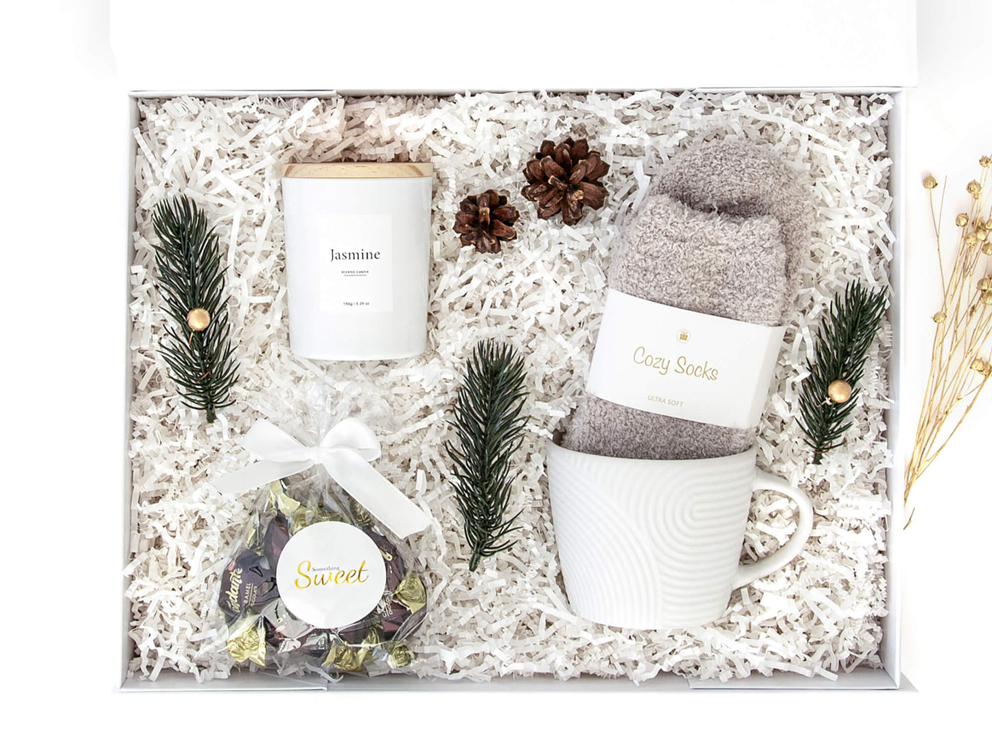 Hvit gaveeske med sokker, sjokolader, duftlys og en hvit kopp. Dekorert med juledekor