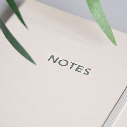 Nærbilde av beige notatbok med sølvfarget NOTES-tekst