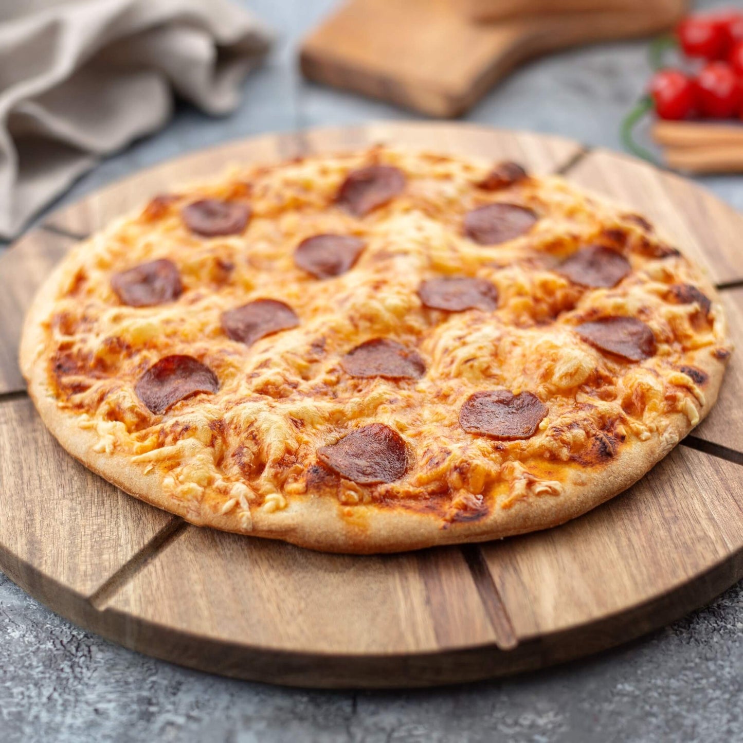 Nystekt pizza med ost og pepperoni på rundt pizzabrett i akasietre