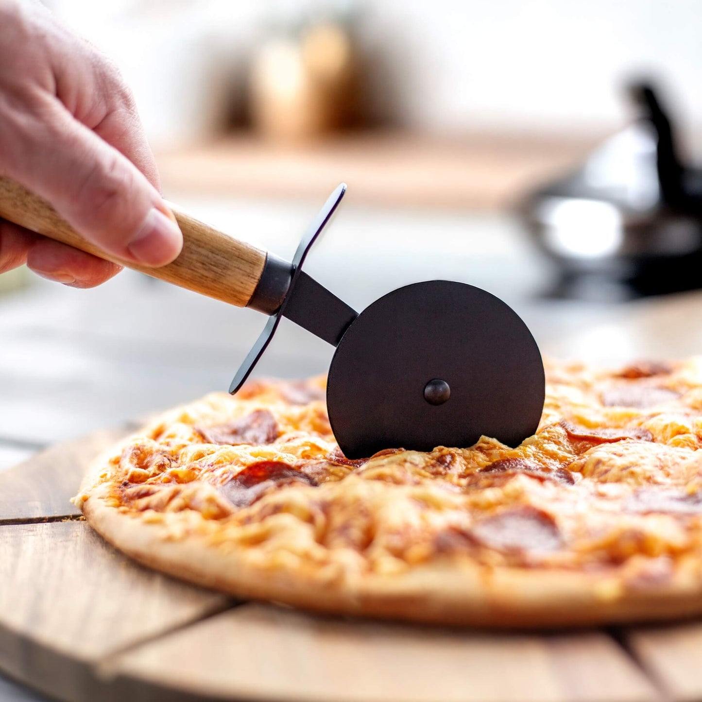 Sort pizzaskjærer med håndtak i akasietre som skjærer en pizza