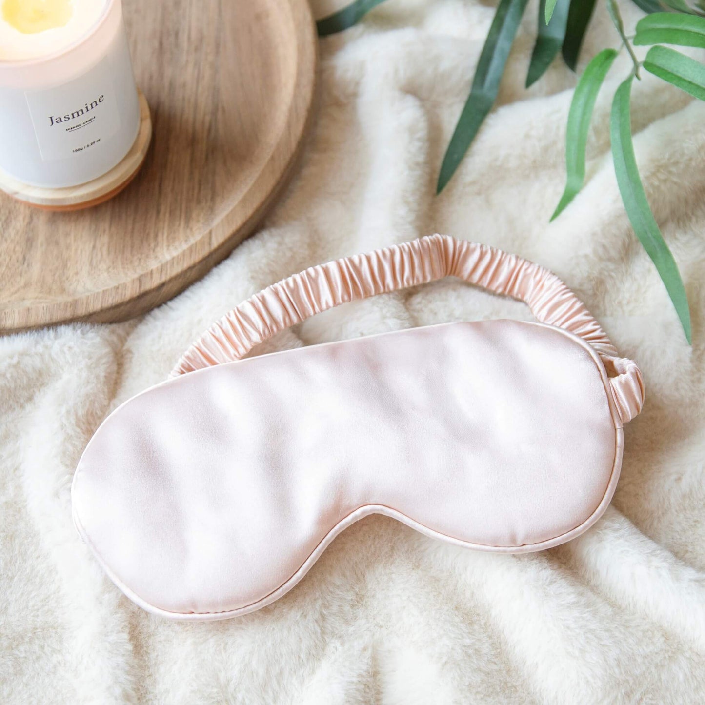 Beige sovemaske i silkemyk sateng ved siden av et tent duftlys
