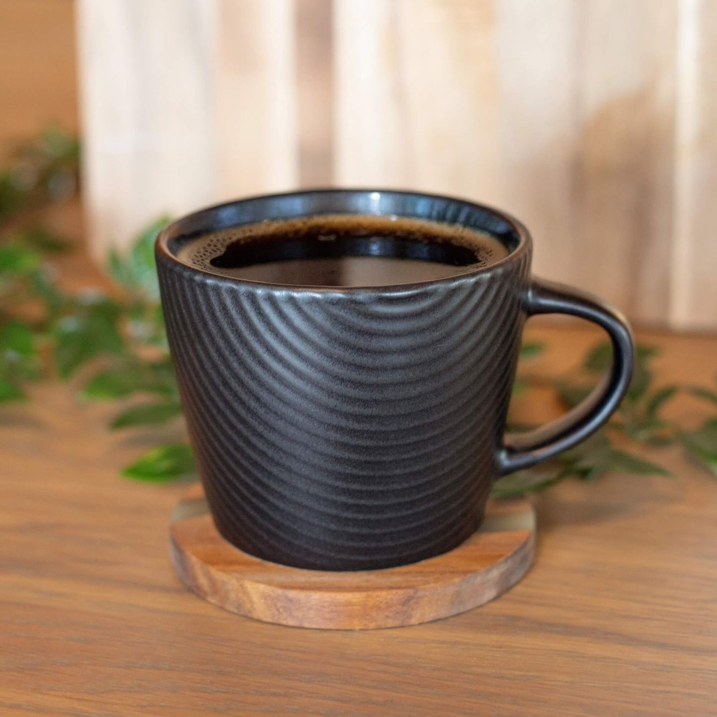 Svart kaffekopp med strukturert mønster på rund bordbrikke i akasietre