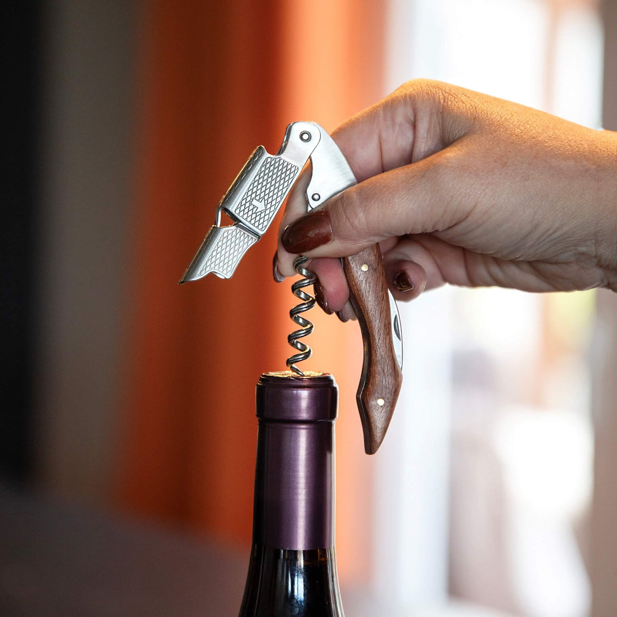 Kelneråpner med trehåndtak i bruk, med to-trinns løftepunkt som trekker korken ut av en vinflaske